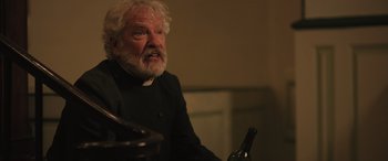 Movie still from “Pet Sematary: Bloodlines” (2023), directed by Lindsey Anderson Beer – An old man with a beard and a white beard is holding a bottle of wine; Close Up shot, Over the shoulder angle