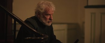 Movie still from “Pet Sematary: Bloodlines” (2023), directed by Lindsey Anderson Beer – An older man sitting at a table looking at something; Close Up shot, Low angle