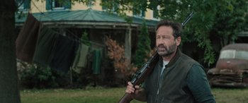 Movie still from “Pet Sematary: Bloodlines” (2023), directed by Lindsey Anderson Beer – A man holding a rifle in a yard; Medium shot, Over the shoulder angle
