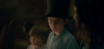 Movie still from “Peter Pan & Wendy” (2023), directed by David Lowery – A young boy wearing a top hat and glasses; Close Up shot, Over the shoulder angle