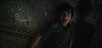 Movie still from “Peter Pan & Wendy” (2023), directed by David Lowery – A boy in a green shirt is leaning against a wall; Medium shot, Low angle