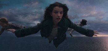 Movie still from “Peter Pan & Wendy” (2023), directed by David Lowery – A woman flying through the air in front of a body of water; Medium shot, Overhead angle