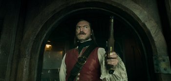 Movie still from “Peter Pan & Wendy” (2023), directed by David Lowery – A man holding a gun while standing in front of an archway; Medium shot, Low angle