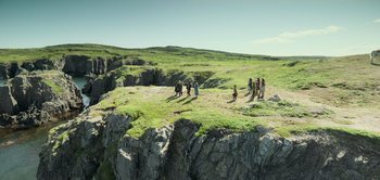 Movie still from “Peter Pan & Wendy” (2023), directed by David Lowery – A group of people standing on top of a grass covered hill; Extreme Wide shot, High angle