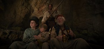 Movie still from “Peter Pan & Wendy” (2023), directed by David Lowery – A group of people sitting in a cave; Medium shot, Low angle