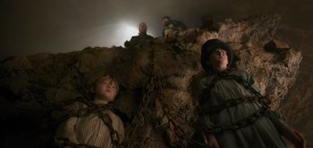 Movie still from “Peter Pan & Wendy” (2023), directed by David Lowery – A group of people sitting on top of a rock; Medium shot, Low angle