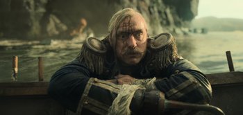 Movie still from “Peter Pan & Wendy” (2023), directed by David Lowery – A man with a beard and mustache is sitting in a boat; Close Up shot, Low angle