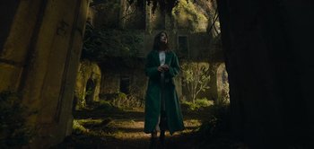 Movie still from “Peter Pan & Wendy” (2023), directed by David Lowery – A man in a green coat standing in front of an abandoned building; Wide shot, Low angle