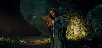 Movie still from “Peter Pan & Wendy” (2023), directed by David Lowery – A woman standing in the woods looking at an open book; Medium shot, Low angle
