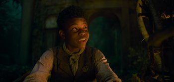 Movie still from “Peter Pan & Wendy” (2023), directed by David Lowery – A young man smiles while sitting in a dark room; Close Up shot, Low angle