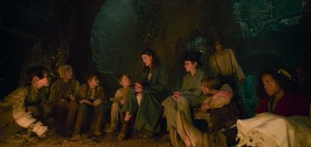Movie still from “Peter Pan & Wendy” (2023), directed by David Lowery – A group of people sitting in a cave; Medium shot, Low angle