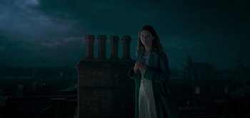 Movie still from “Peter Pan & Wendy” (2023), directed by David Lowery – A woman standing in front of a bunch of chimneys at night; Medium shot, Low angle