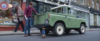Movie still from “Peter Rabbit 2: The Runaway” (2021), directed by Will Gluck – A small dog standing next to an old green truck; Wide shot, Low angle