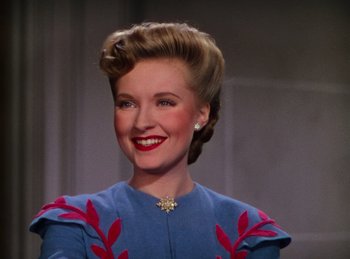 Movie still from “Phantom of the Opera” (1943), directed by Arthur Lubin – A woman in a blue and red dress smiling for the camera; Close Up shot, Over the shoulder angle