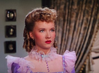 Movie still from “Phantom of the Opera” (1943), directed by Arthur Lubin – A woman in a purple dress with a red bow in her hair; Close Up shot, Over the shoulder angle