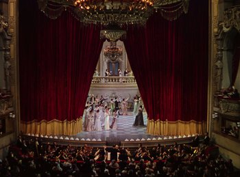 Movie still from “Phantom of the Opera” (1943), directed by Arthur Lubin – A large crowd of people are gathered in front of a stage with red drapes; Extreme Wide shot, High angle