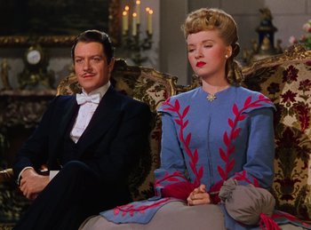 Movie still from “Phantom of the Opera” (1943), directed by Arthur Lubin – A man and a woman sitting on a couch in a room; Medium shot, Low angle
