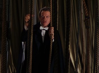 Movie still from “Phantom of the Opera” (1943), directed by Arthur Lubin – A man in a tuxedo standing in a room with ropes; Medium shot, Low angle