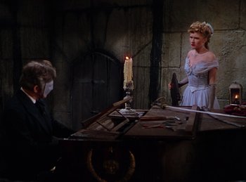 Movie still from “Phantom of the Opera” (1943), directed by Arthur Lubin – A man and a woman standing in front of a table; Wide shot, High angle