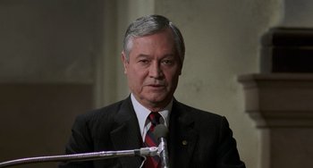 Movie still from “Philadelphia” (1993), directed by Jonathan Demme – An older man wearing a suit and tie while standing at a microphone; Close Up shot, High angle