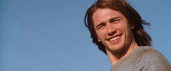 Movie still from “Pineapple Express” (2008), directed by David Gordon Green – A person with long brown hair smiling; Close Up shot, Low angle