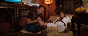 Movie still from “Pineapple Express” (2008), directed by David Gordon Green – A man sitting on the floor while another man lays on the floor; Medium shot, Low angle