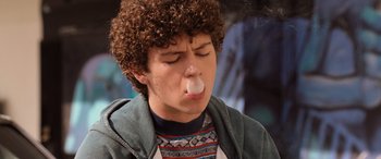 Movie still from “Pineapple Express” (2008), directed by David Gordon Green – A young man with curly hair is smoking a cigarette in his mouth; Close Up shot, Low angle
