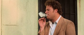 Movie still from “Pineapple Express” (2008), directed by David Gordon Green – A man in a brown jacket smoking a cigarette; Medium shot, Overhead angle