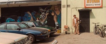 Movie still from “Pineapple Express” (2008), directed by David Gordon Green – A man standing next to a car parked in front of a mural; Wide shot, Low angle