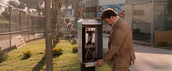 Movie still from “Pineapple Express” (2008), directed by David Gordon Green – A man in a brown suit is looking at a payphone; Wide shot, High angle