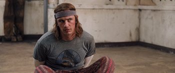 Movie still from “Pineapple Express” (2008), directed by David Gordon Green – A man sitting on the ground wearing a headband; Close Up shot, Over the shoulder angle