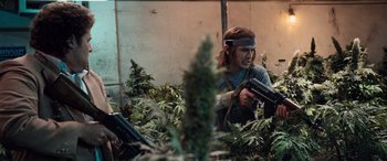 Movie still from “Pineapple Express” (2008), directed by David Gordon Green – A man holding a gun while standing next to marijuana plants; Medium shot, Low angle