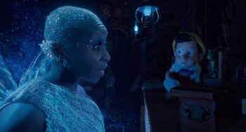 Movie still from “Pinocchio” (2022), directed by Robert Zemeckis – A woman standing in front of a doll in a dark room; Medium shot, Over the shoulder angle