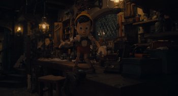 Movie still from “Pinocchio” (2022), directed by Robert Zemeckis – A doll is standing on a table in a dark room; Wide shot, High angle