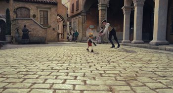 Movie still from “Pinocchio” (2022), directed by Robert Zemeckis – A man and a boy are playing a game on a brick road; Wide shot, High angle