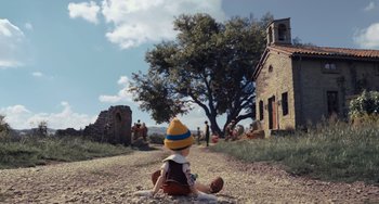 Movie still from “Pinocchio” (2022), directed by Robert Zemeckis – A child sitting on the ground in front of an old building; Extreme Wide shot, High angle