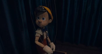 Movie still from “Pinocchio” (2022), directed by Robert Zemeckis – A pinocchio puppet is being held up by strings; Close Up shot, High angle