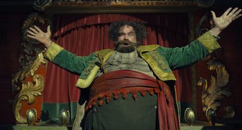 Movie still from “Pinocchio” (2022), directed by Robert Zemeckis – A man with a beard and mustache wearing a green jacket; Medium shot, Low angle