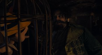 Movie still from “Pinocchio” (2022), directed by Robert Zemeckis – A man with a beard is looking through a cage; Close Up shot, Over the shoulder angle