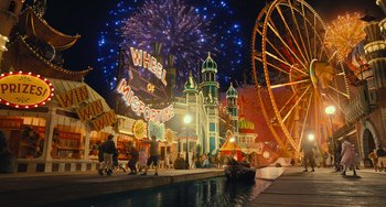 Movie still from “Pinocchio” (2022), directed by Robert Zemeckis – A group of people walking around a carnival area at night with fireworks in the background; Extreme Wide shot, High angle