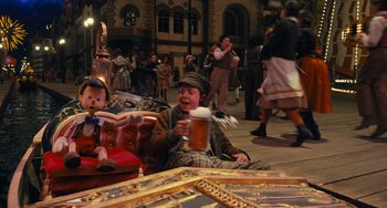 Movie still from “Pinocchio” (2022), directed by Robert Zemeckis – A man sitting on the ground holding a mug of beer; Wide shot, High angle