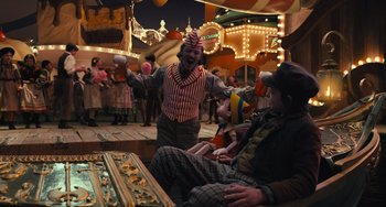Movie still from “Pinocchio” (2022), directed by Robert Zemeckis – Two clowns sitting on a bench at a carnival; Wide shot, High angle