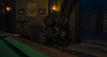 Movie still from “Pinocchio” (2022), directed by Robert Zemeckis – A man sitting on a chair next to a wooden barrel; Wide shot, High angle