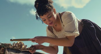 Movie still from “Pinocchio” (2022), directed by Robert Zemeckis – A woman in white shirt and black skirt holding a stick; Medium shot, Low angle