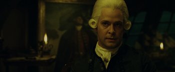 Movie still from “Pirates of the Caribbean: At World's End” (2007), directed by Gore Verbinski – A man in a wig and a wig stand in front of a painting; Close Up shot, Over the shoulder angle