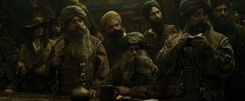 Movie still from “Pirates of the Caribbean: At World's End” (2007), directed by Gore Verbinski – A group of men sitting at a table with a mug; Medium shot, Over the shoulder angle