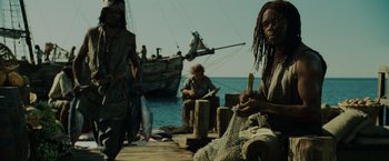 Movie still from “Pirates of the Caribbean: Dead Man's Chest” (2006), directed by Gore Verbinski – A group of people sitting on a dock with a boat in the background; Medium shot, Low angle
