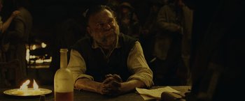 Movie still from “Pirates of the Caribbean: Dead Man's Chest” (2006), directed by Gore Verbinski – An old man sitting at a table with his hands clasped together; Medium shot, Low angle