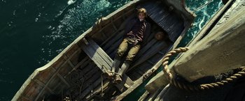 Movie still from “Pirates of the Caribbean: Dead Men Tell No Tales” (2017), directed by Espen Sandberg – A man laying in a wooden boat in the water; Wide shot, Overhead angle