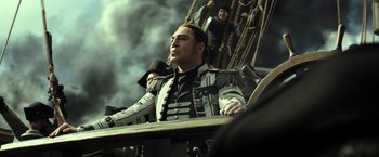 Movie still from “Pirates of the Caribbean: Dead Men Tell No Tales” (2017), directed by Espen Sandberg – A man sitting on top of a boat in the middle of the ocean; Medium shot, Low angle